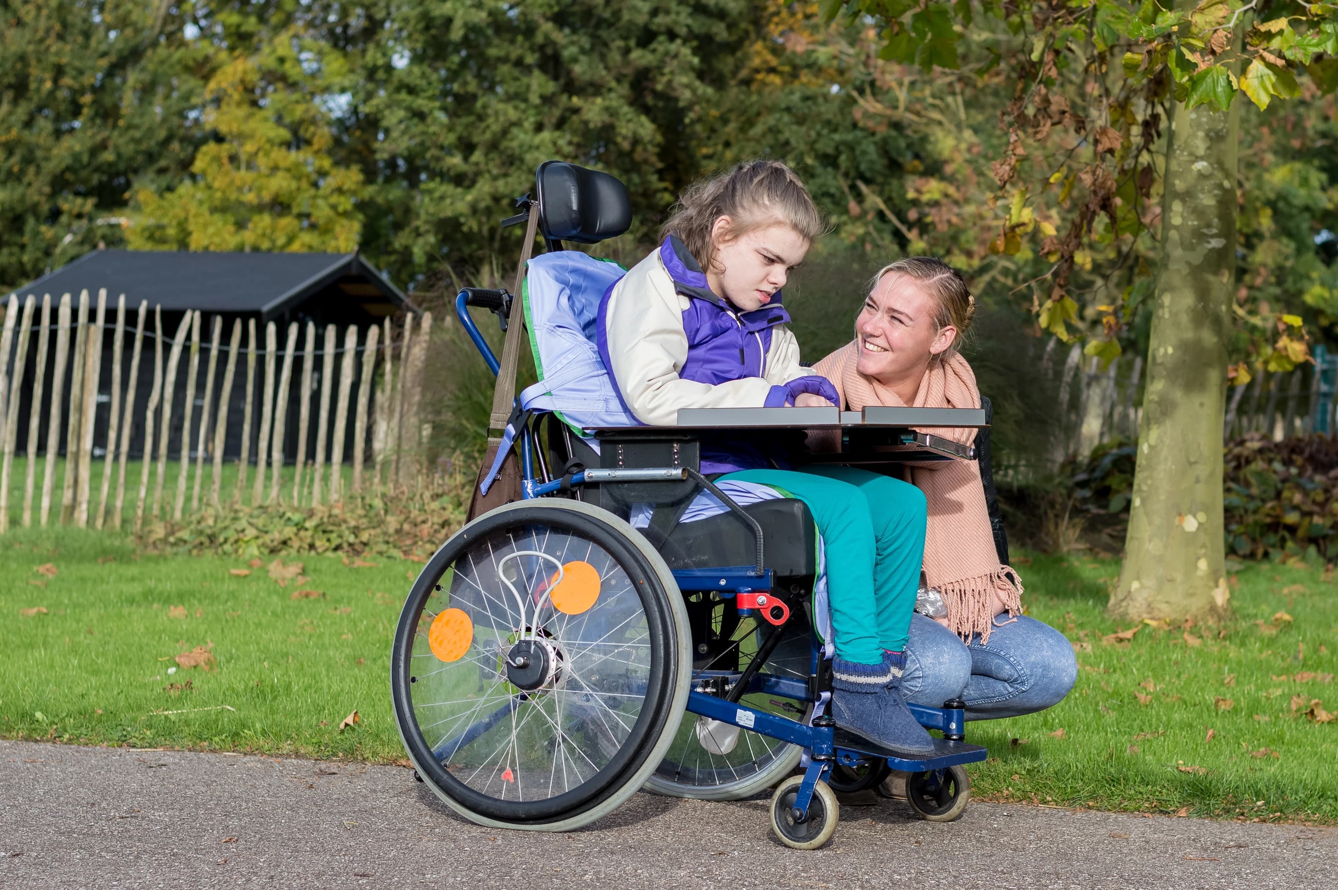 Caregiver smiling with a child in a wheelchair outdoors